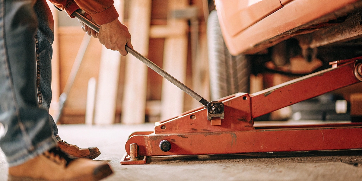 A person safely using a screw jack to lift a heavy machine part.